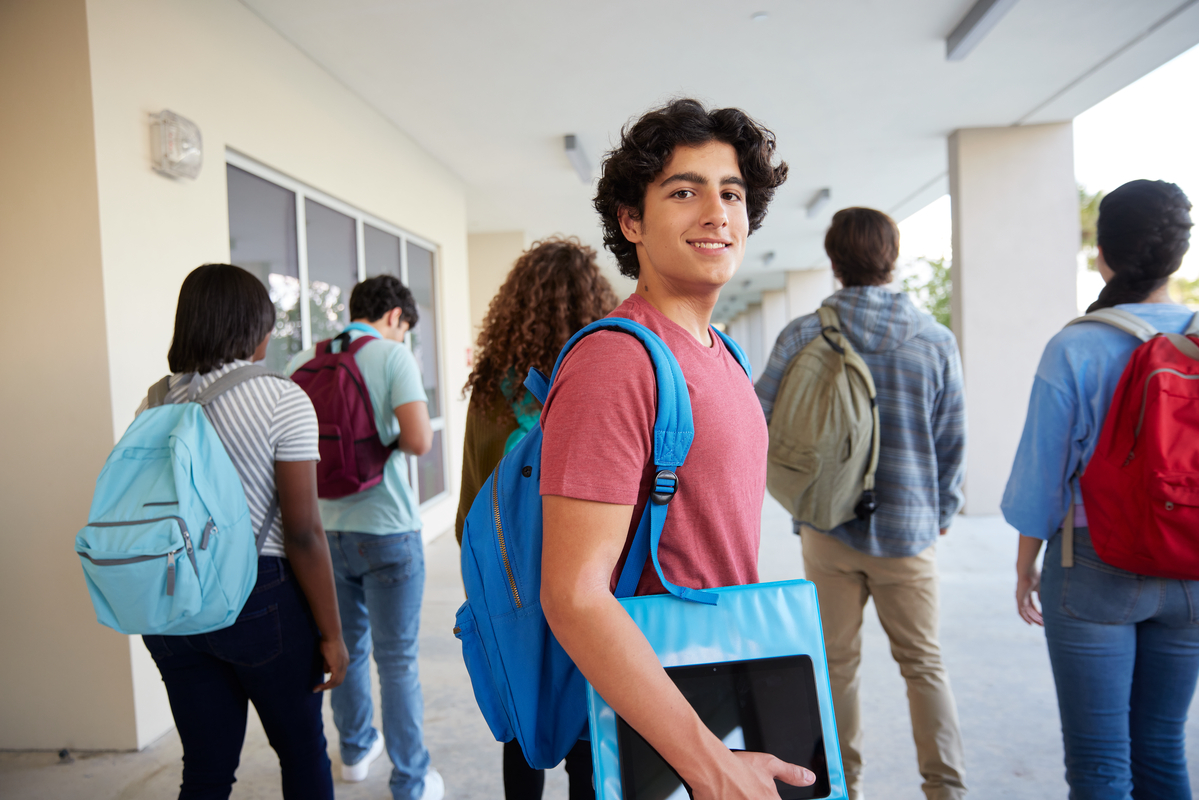 young man facing the camera, standing while other students are walking down the school hallway
